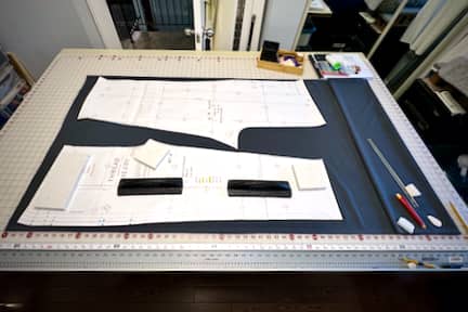 Grey fabric lies on a large cutting table with pattern pieces lying on top, waiting to be traced out.